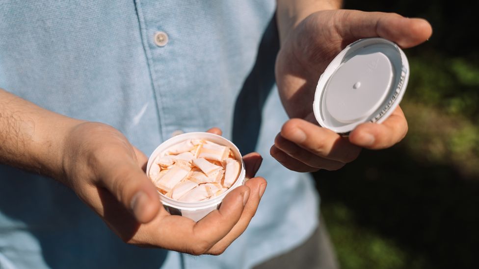 Mužské ruce držící otevřenou krabičku s nikotinovými sáčky, v pozadí modrá košile