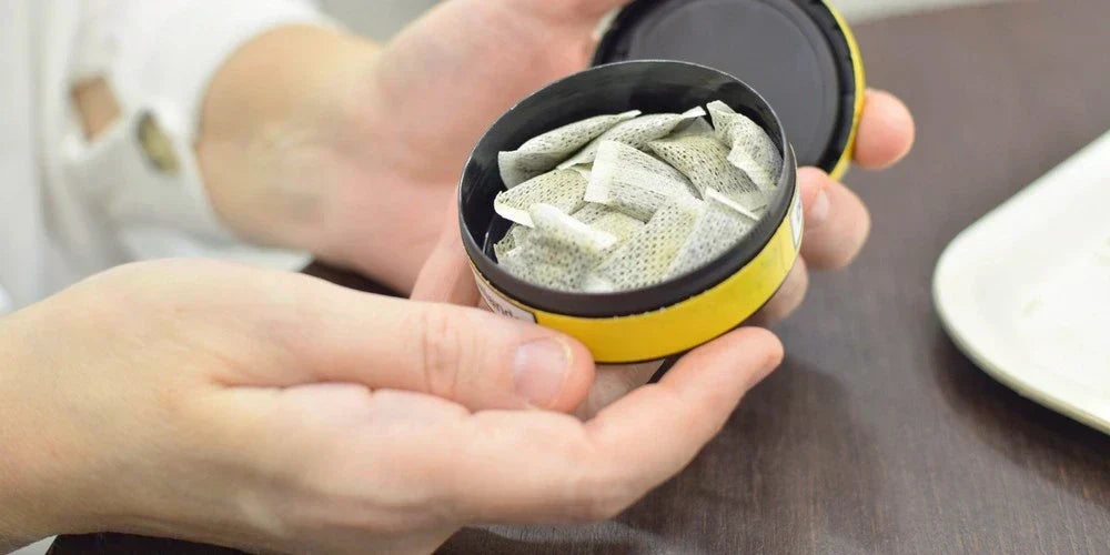 chlapská ruka drží otevřenou krabičku nikotinových sáčků s viditelnými sáčky uvnitř