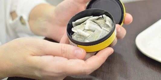 chlapská ruka drží otevřenou krabičku nikotinových sáčků s viditelnými sáčky uvnitř